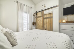 A bedroom with a large bed, a wooden wardrobe, a mounted TV, and a window with curtains.