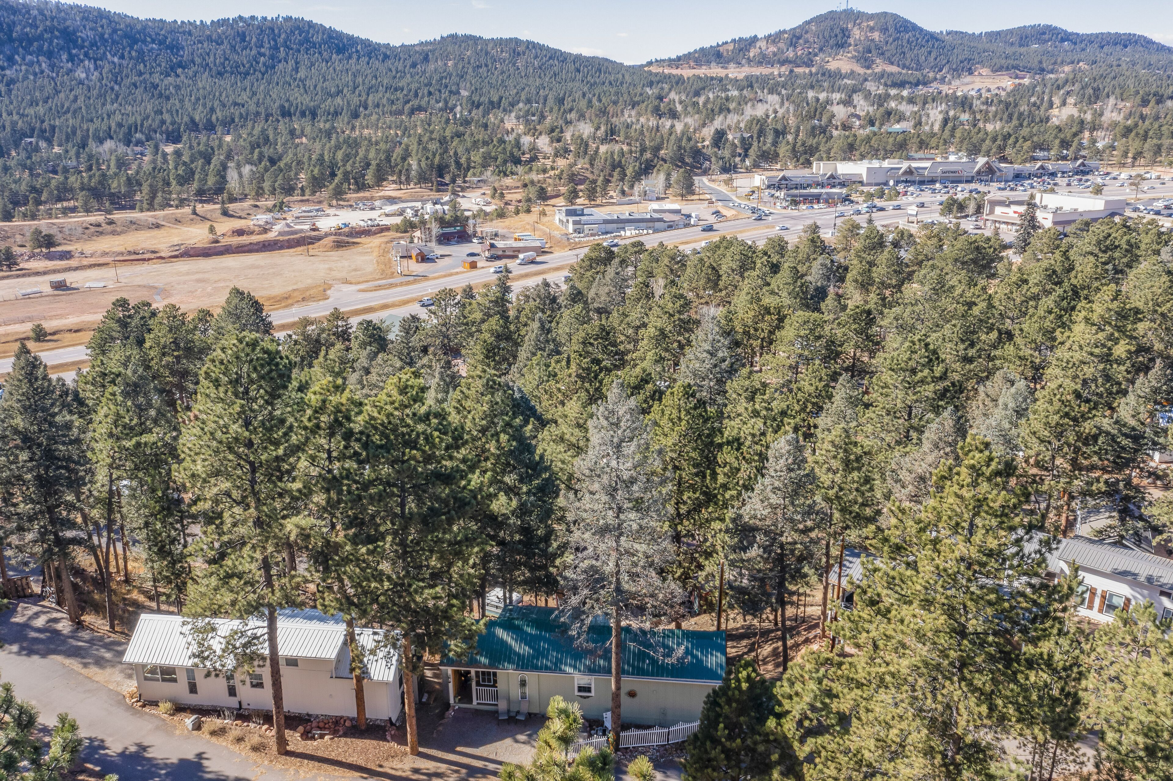 A remote cabin surrounded by dense forest, with a clear road leading to a commercial area in the background.
