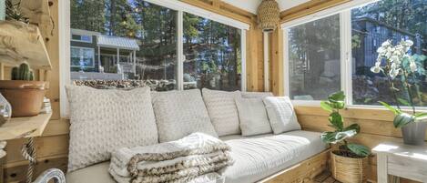 A cozy wooden cabin with a large window, a cushioned bench, and a rustic interior.