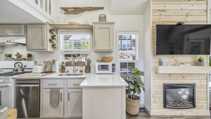 A modern kitchen with white cabinetry, a central island, a built-in microwave, and a fireplace. - Biggie Smalls (Woodland Park)