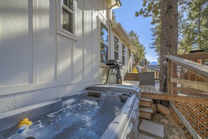 A hot tub adjacent to a building with a wooden deck and steps leading to a covered area.