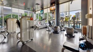 A modern gym with various exercise equipment, large windows, and a view of the city. - Upper Studio with Stunning Views + Pool + Gym (Hallandale Beach)