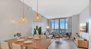 A modern living room with a dining area, large windows, and a TV.