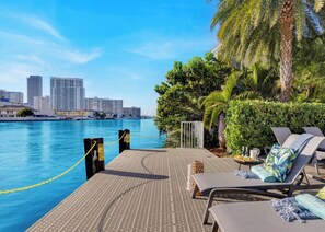 A waterfront deck with lounge chairs, a pool, and a city skyline in the background.