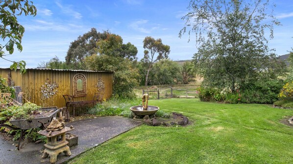 A rustic garden with a metal bench, a decorative fountain, and a corrugated metal shed.