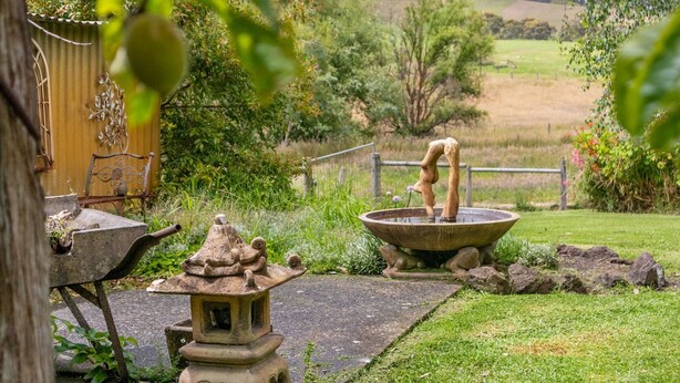 Un jardín con una fuente de piedra, una casa de té tradicional japonesa y una estructura de madera rústica.