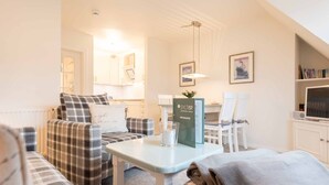 A cozy living room with a sofa, chairs, a coffee table, and a TV. There is a sign on the table and a framed picture on the wall. - 2-room apartment close to the beach, approx. 45 m² living space, for 2 people (Wenningstedt-Braderup (Sylt))