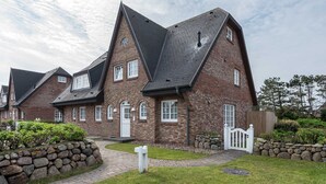A row of brick houses with steeply pitched roofs and white trim, surrounded by a well-maintained garden and a stone wall. - 2-room apartment close to the beach, approx. 45 m² living space, for 2 people (Wenningstedt-Braderup (Sylt))