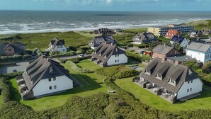 Ein Küstendorf mit traditionellen weißen Häusern, einem Strand und einem modernen Gebäude im Hintergrund.