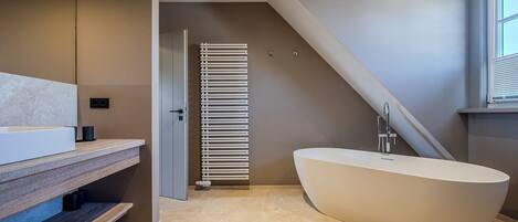 A modern bathroom with a freestanding bathtub, a wooden vanity, and a towel rack.