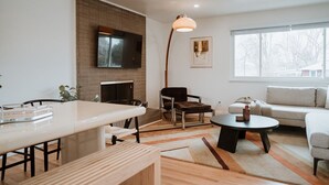 A modern living room with a fireplace, a dining table, a sofa, and a large window. - Hot Tub House with BBQ Deck and Workspace (Centennial)