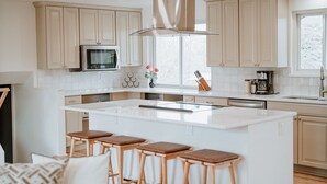 A modern kitchen with a large island, wooden stools, a microwave, and a window with a view. - Hot Tub House with BBQ Deck and Workspace (Centennial)