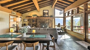 A spacious living area with a stone fireplace, wooden ceiling beams, and large windows offering mountain views.