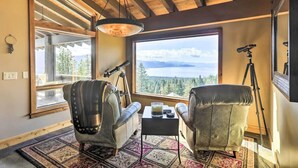 A cozy room with a large window, two leather chairs, a small table with a drink, and a telescope on a tripod.
