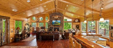 A spacious living area with a fireplace, wooden ceiling, and large windows.