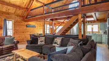 Ein Holzblockhaus-Interieur mit Wohnzimmer, Essbereich, Küche und einer Treppe.