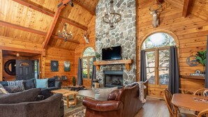 A log cabin interior with a stone fireplace, wooden furniture, and a mounted deer head. - Stunning and Expansive 15 bedrooms Situated Close to Ski Slopes (McGaheysville)