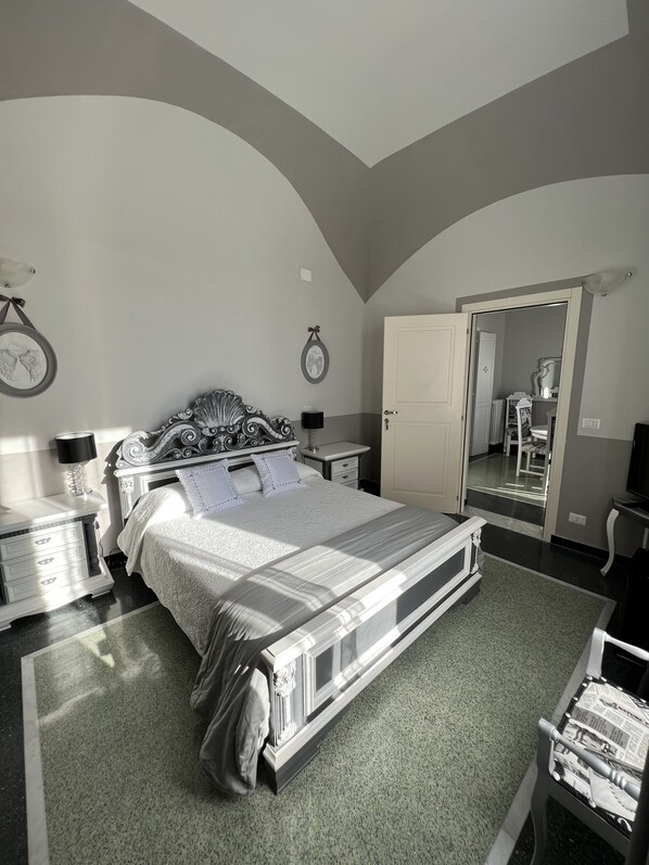 A bedroom with a large bed, a nightstand, a dresser, a mirror, and a door leading to another room. - B&B VILLA PRESTIGIO (Novi Ligure)