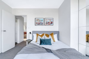 A modern hotel room with a large bed, a bedside table, and two framed pictures on the wall.