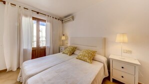 Una cama doble con dos almohadas, una mesita de noche con lámpara y una ventana con cortinas.