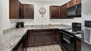 A kitchen with dark wood cabinets, a granite countertop, a stainless steel refrigerator, a black microwave, and a stove. - 6A Family Friendly RedCliff Condo POOL & HOT TUB (Moab)