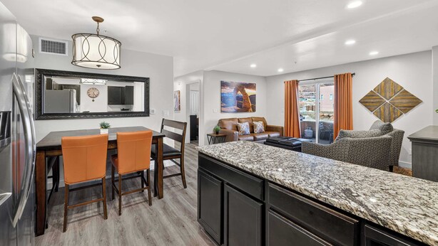 A modern kitchen with a granite countertop, dark cabinetry, and a dining area with orange chairs. - 6A Family Friendly RedCliff Condo POOL & HOT TUB (Moab)