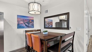 A dining area with a wooden table, four chairs, a small plant, and two wall-mounted paintings. - 6A Family Friendly RedCliff Condo POOL & HOT TUB (Moab)