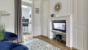 Een moderne woonkamer met een open haard, televisie en een blauwe fauteuil.