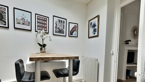Een moderne eethoek met een houten tafel en zwarte stoelen, een vaas met witte bloemen en stadsgezichten in lijstjes aan de muur.
