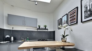 Een moderne keuken met grijze kastjes, een houten aanrechtblad en een zwarte spatwand. Op het aanrechtblad staan twee potten met planten en aan de muur hangt een lijst met een foto.