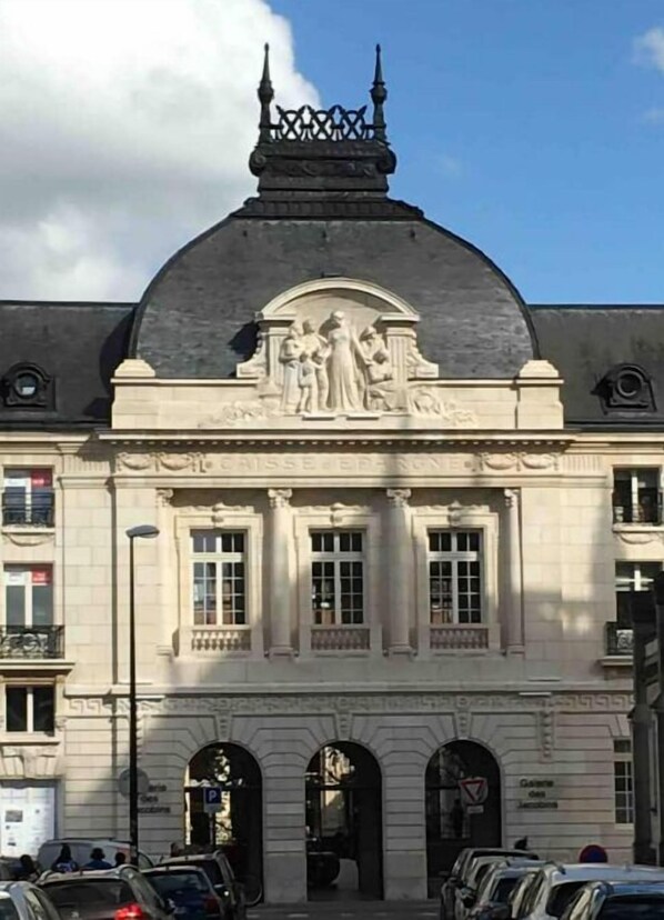 Ein klassizistisches Gebäude mit einem zentralen Giebel und einem Relief, großen Fenstern und einer symmetrischen Fassade.
