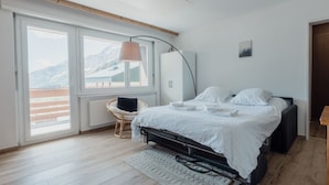 Ein Schlafzimmer mit Bett, Stuhl, Kleiderschrank und Bergblick durch große Fenster.
