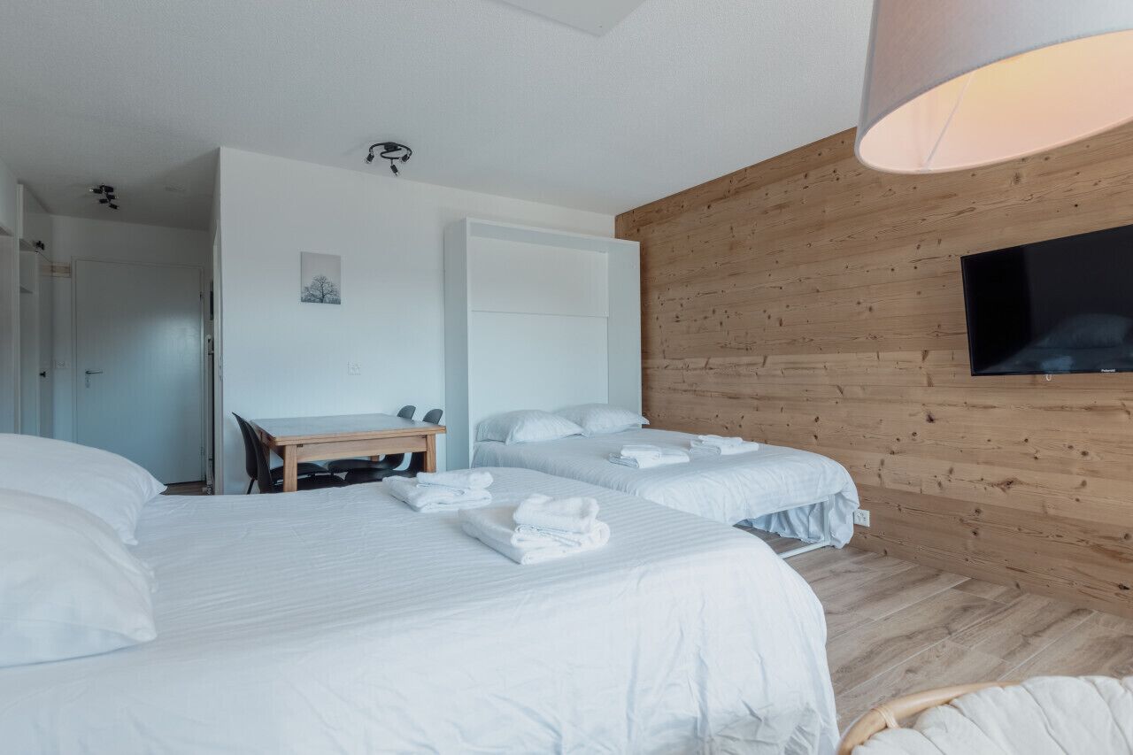 A hotel room with two beds, a desk, and a TV.