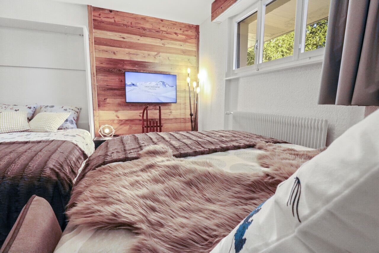 Un dormitorio con dos camas, una pared decorativa de madera, un televisor y una ventana con cortinas.