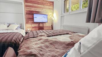 Un dormitorio con dos camas, una pared decorativa de madera, un televisor y una ventana con cortinas.