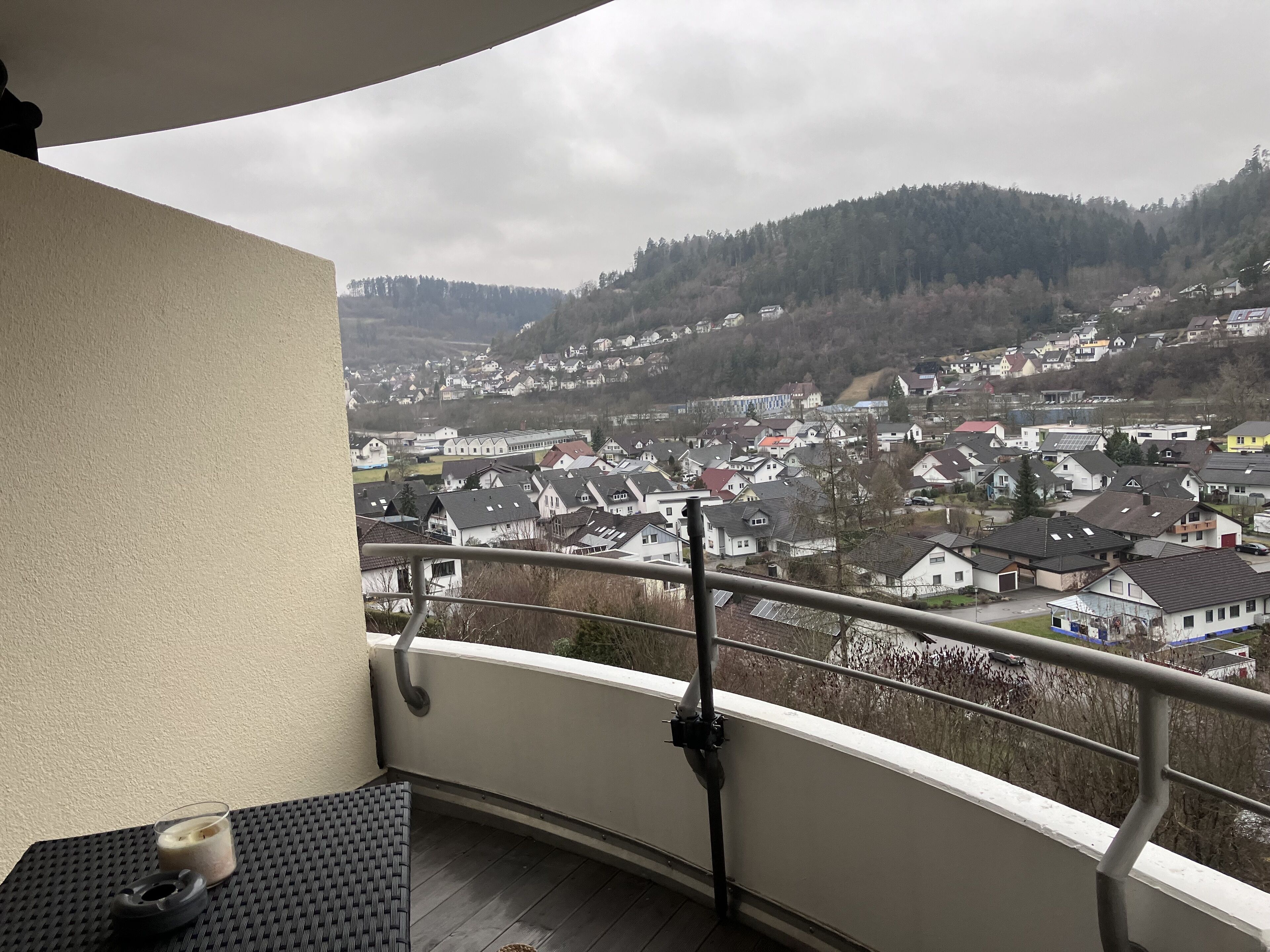 Un balcon donnant sur un quartier résidentiel, un verre de lait et une chaise noire.
