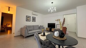 Un salon moderne avec un canapé gris, une table basse noire, un téléviseur et un lustre.