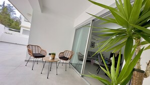 Une terrasse extérieure moderne, avec deux fauteuils en osier et une petite table, un pot de fleurs et une porte-fenêtre coulissante donnant sur un espace intérieur.