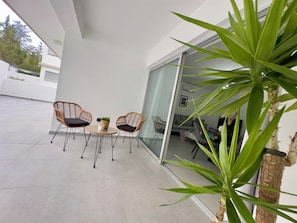 A modern outdoor patio with two wicker chairs, a small table, and a potted plant.