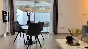 Un salon moderne comprenant un coin repas, de grandes portes-fenêtres coulissantes donnant sur un balcon, une cuisine avec un four encastré et un canapé blanc.