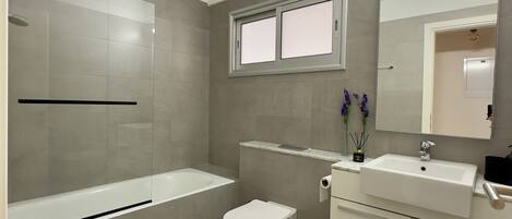 A modern bathroom with a bathtub, toilet, and vanity with a mirror.
