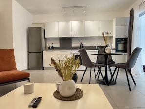 A modern kitchen with white cabinets, a refrigerator, and a dining area with chairs and a table.