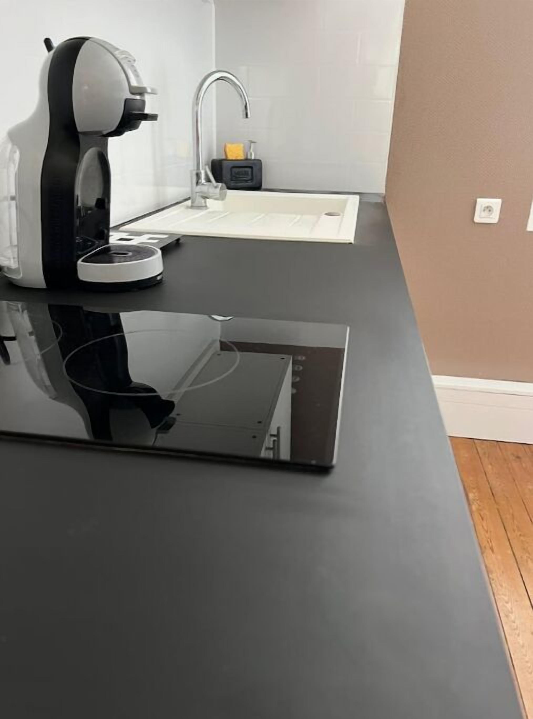 Une cuisine avec un plan de travail noir, une machine à café et un évier.