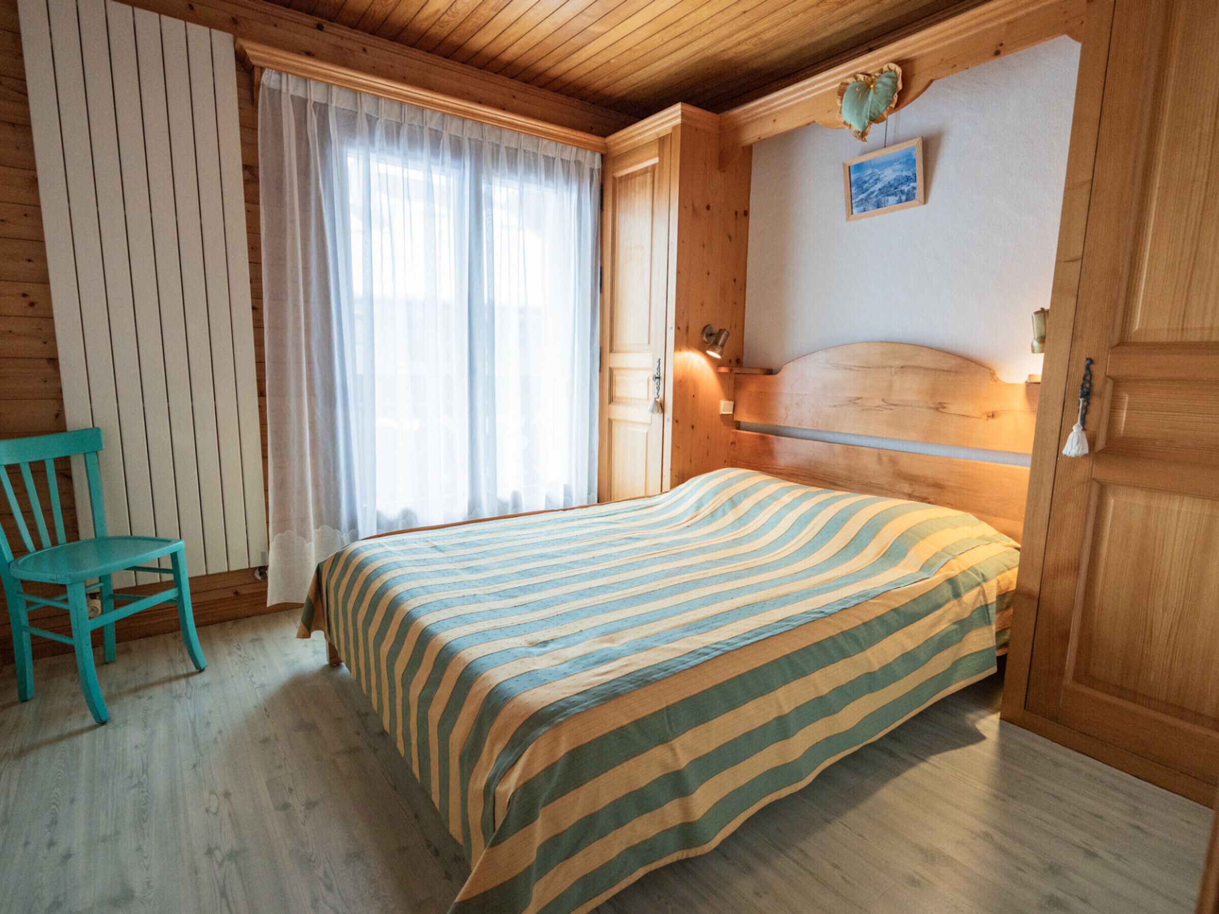 A cozy room with a wooden bed, a chair, and a window with curtains.
