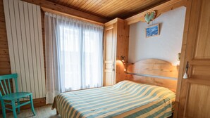 A cozy room with a wooden bed, a chair, and a window with curtains. - Charming 1BR Apt, Balcony, Wi-Fi, Near Ski Lifts - Pets Welcome! (Les Gets)