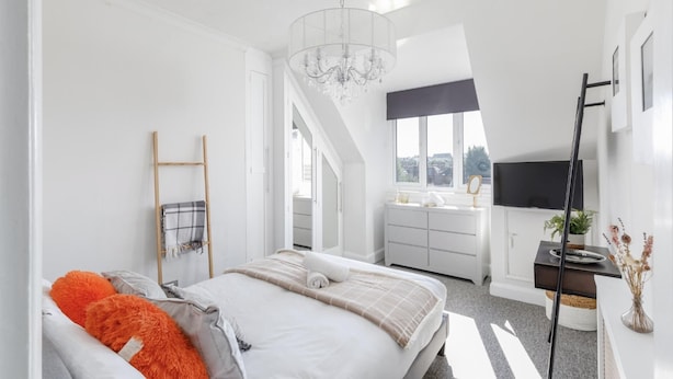 A modern bedroom with a bed, a chandelier, a TV, and a staircase leading to another room. - Immaculate 2-bed Apartment in Hove (Hove)