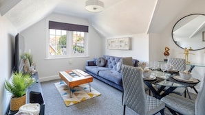 A modern loft apartment with a high ceiling, a blue sofa, a glass dining table, and a large window offering a city view. - Immaculate 2-bed Apartment in Hove (Hove)