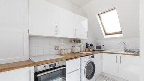 A modern kitchen with white cabinets, a wooden countertop, a built-in oven, a washing machine, a microwave, and a skylight. - Immaculate 2-bed Apartment in Hove (Hove)