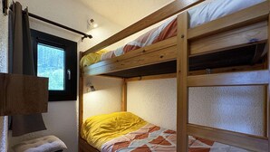 Un lit superposé avec une fenêtre, un petit tabouret et un luminaire fixé au mur.