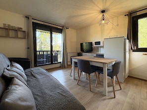 A compact living space with a sofa, a dining table with chairs, a TV, and a refrigerator.